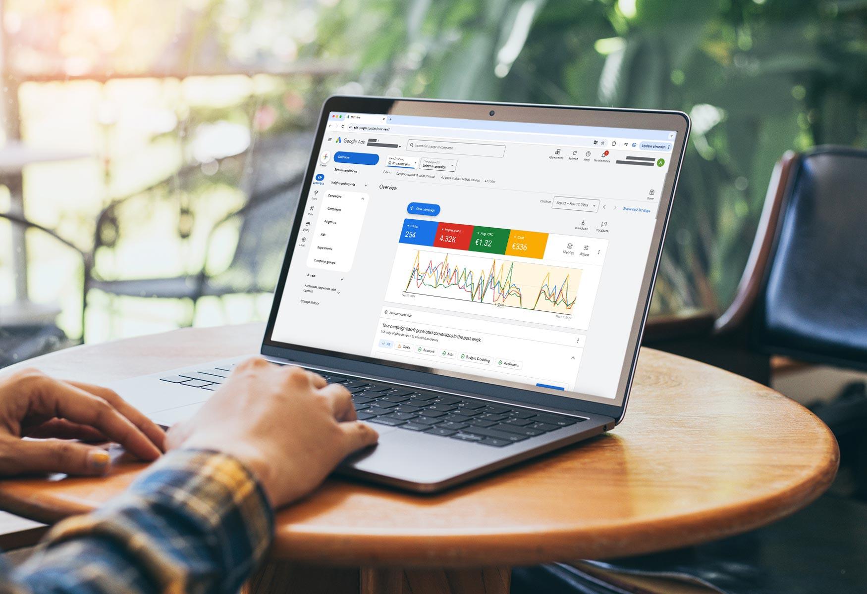 Laptop op tafel met Google Ads dashboard zichtbaar, inclusief grafieken en campagneprestaties in een werkomgeving.